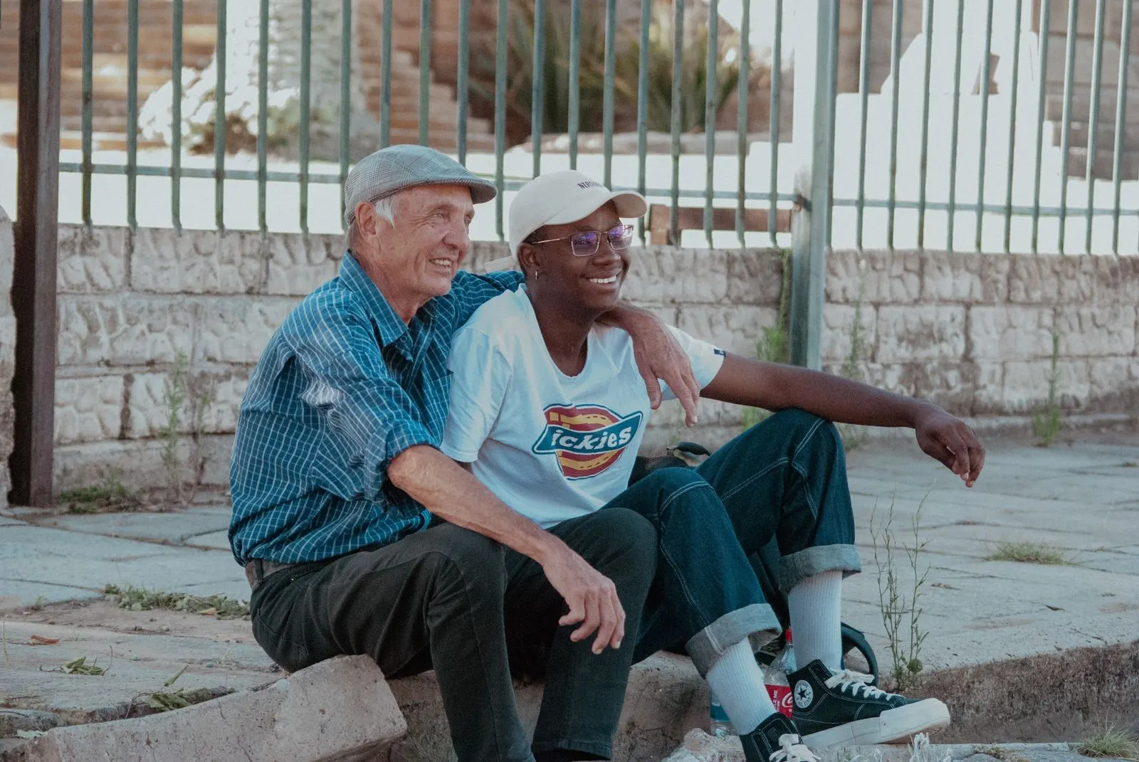 An older man and a younger friend sitting side by side outdoors, both smiling
